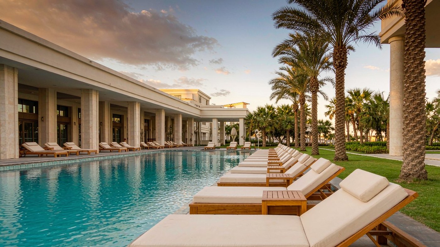 Resort pool deck lined with teak sun loungers and palm trees at golden hour